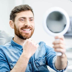 Mann lächelt mit Spiegel beim Zahnarzt