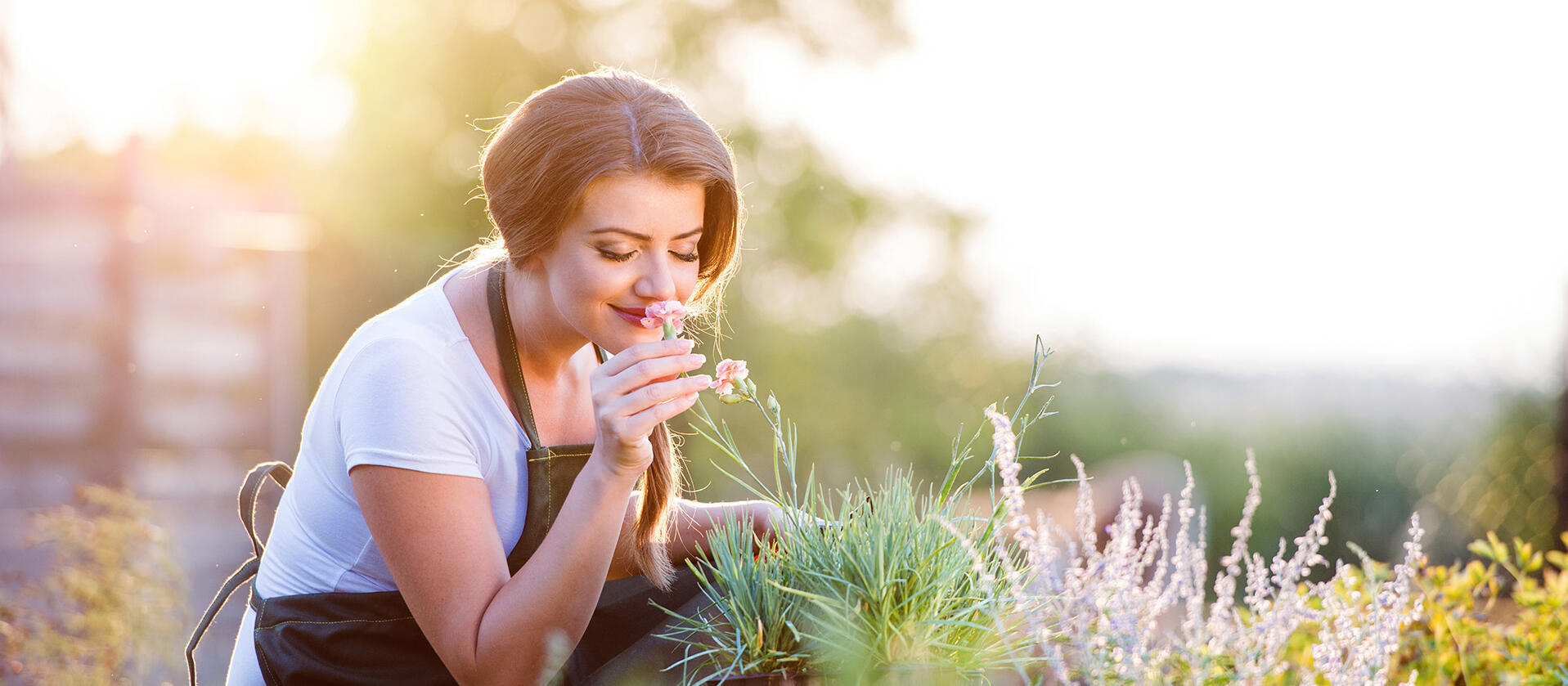 Frau sitzt auf einer Wiese in der Natur und riecht an einer Pflanze