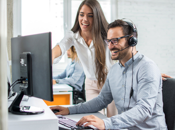 Frau und Mann mit Headset vor Bildschirm