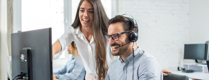 Frau und Mann mit Headset vor Bildschirm