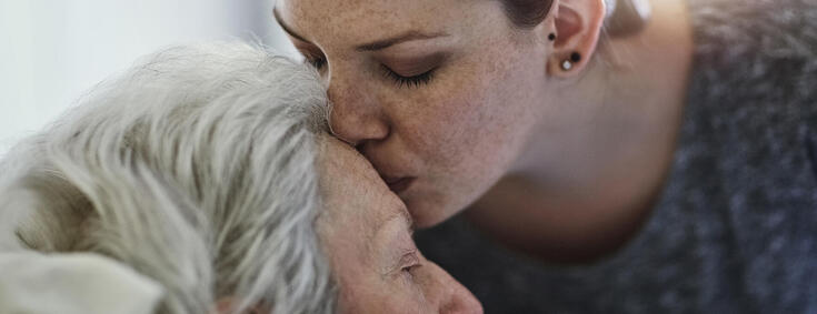 Junge Frau küsst ältere Frau im Krankenbett auf die Stirn