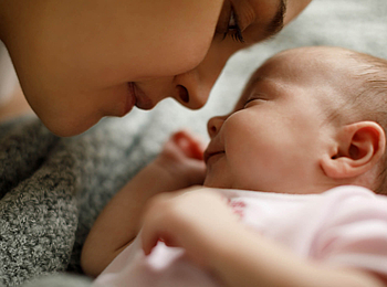 Eine junge Mutter beugt sich nah zu ihrem Baby, sie lächelt. Das Baby hat die Augen geschlossen. 