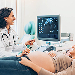 Eine Ärztin macht einen Bauch-Ultraschall bei einer schwangeren Frau. Beide Frauen lächeln.