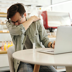 Ein Mann niest in einem Café, während sie an einem Laptop arbeitet.
