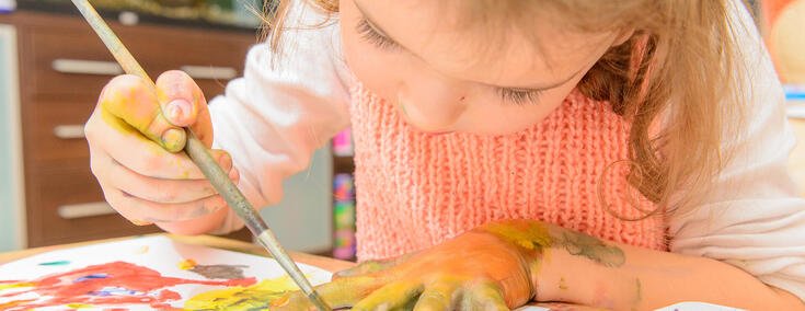 Kleines Mädchen spielt mit Farben und bemalt Papier und Hand