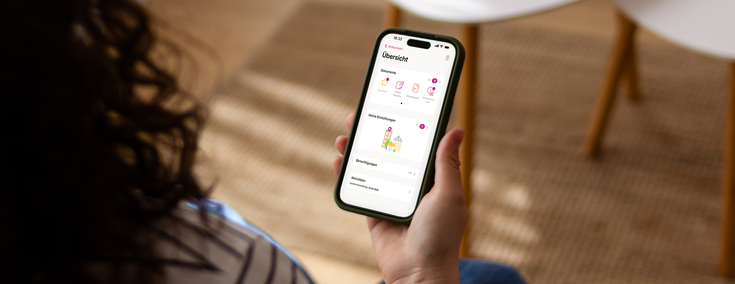 Eine Frau mit lockigen Haaren sitzt in ihrem Wohnzimmer. Auf ihrem Smartphone nutzt sie die ePA App.