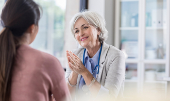Eine ältere Hausärztin mit kurzen grauen Haaren führt ein Arztgespräch mit einer Patientin. Sie lächelt dabei freundlich.