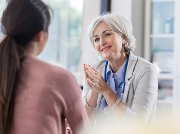 Eine ältere Hausärztin mit kurzen grauen Haaren führt ein Arztgespräch mit einer Patientin. Sie lächelt dabei freundlich.