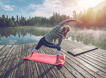 Eine junge Frau macht im Rahmen der Aktivwoche Yoga-Übungen an einem See.