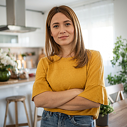 Eine junge Frau mit langen braunen Haaren schaut lächelnd in die Kamera.