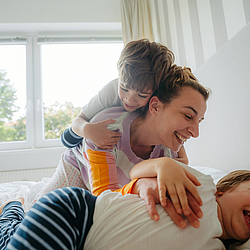 Eine Mutter kuschelt mit ihren beiden Kindern im Bett.