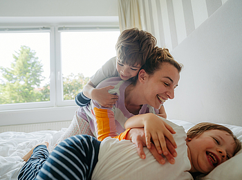 Eine Mutter kuschelt mit ihren beiden Kindern im Bett.