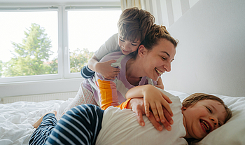 Eine Mutter kuschelt mit ihren beiden Kindern im Bett.