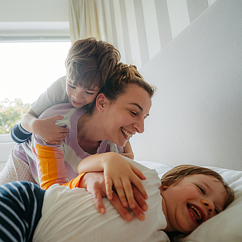 Eine Mutter kuschelt mit ihren beiden Kindern im Bett.