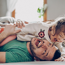 Vater und Tochter toben auf dem Boden.
