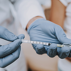 Hände mit Handschuhen ziehen eine Spritze auf.