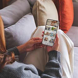Eine Frau mit roten langen Haaren sitzt auf dem Sofa. Sie benutzt die BKK GS-App auf ihrem Smartphone. 