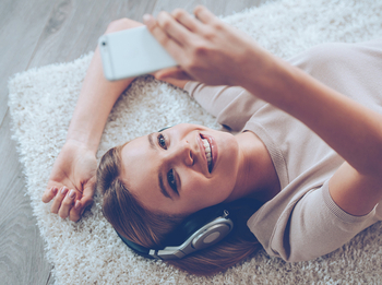 Frau mit Headset und Smartphone in der Hand liegt auf Teppich