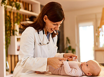 Ein kleines Baby wird von einer Kinderärztin untersucht. Das Baby schaut die Ärztin an und sie lächelt.