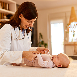 Ein kleines Baby wird von einer Kinderärztin untersucht. Das Baby schaut die Ärztin an und sie lächelt.