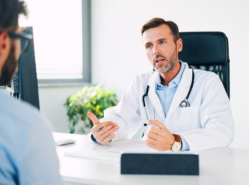 Ein Arzt sitzt an seinem Schreibtisch und klärt seinen Patienten über die Prostatakrebsvorsorge auf.