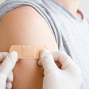 Hände in weißen Handschuhen kleben, nach einer Impfung, ein Pflaster auf den Oberarm eines Patienten.
