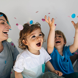 Eine Familie wirft Konfetti in die Luft. Alle haben fröhliche Gesichter.