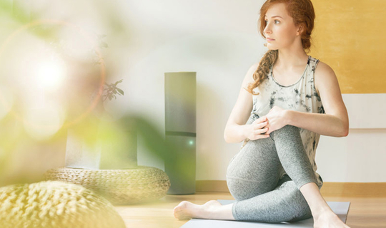Eine junge Frau mit langen lockigen Haaren sitzt in Sportkleidung auf einer Yogamatte. Sie macht eine Hatha-Yoga-Pose.