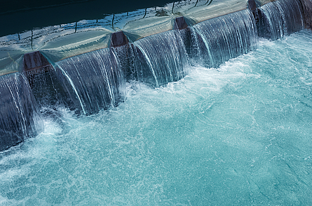 Wasser strömt über die Kante eines Wehrs und schäumt darunter auf.