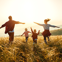 Eine Familie läuft bei Sonnenschein über eine Wiese.