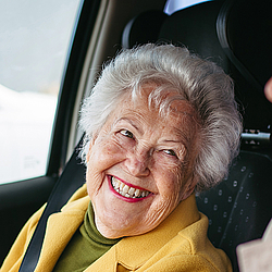 Eine ältere Frau mir kurzen grauen Haaren und eine junge Frau mit schulterlangen hellen Haaren sitzen in Auto und schauen sich an.