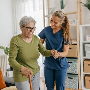Pflegerin hilft älterer Dame mit Gehstock