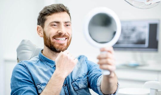 Mann lächelt in Spiegel beim Zahnarzt
