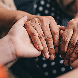 Eine junge Frau hält die Hände einer ältere Frau.