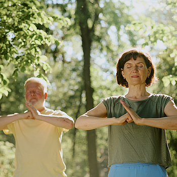 Ein Mann und Frau stehen im Park und machen Qigong.