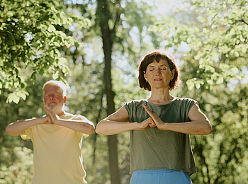 Ein Mann und Frau stehen im Park und machen Qigong.