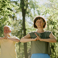 Ein Mann und Frau stehen im Park und machen Qigong.
