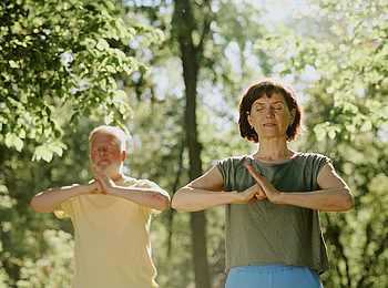 Ein Mann und Frau stehen im Park und machen Qigong.