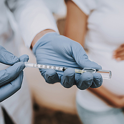 Hände in blauen Handschuhen ziehen eine Spritze mit einer Impfdosis auf.