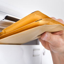 Eine Person steckt mehrere kleine Versandumschläge in einen weißen Briefkasten.