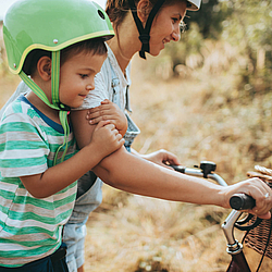 Eine Frau schiebt ihr Fahrrad. Auf dem Sattel sitzt ihr kleiner Sohn.