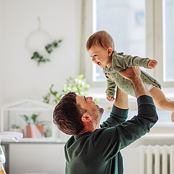 Ein Vater hebt sein Baby in die Luft. Sie lachen beide uns habe Spaß.