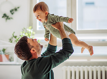 Ein Vater hebt sein Baby in die Luft. Sie lachen beide uns habe Spaß.