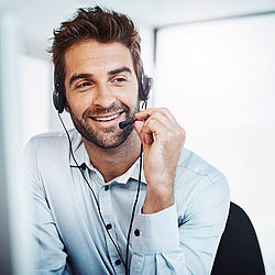 Ein Kundenberater mit braunen Haaren und Bart spricht lächelnd in ein Headset.