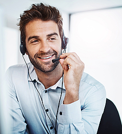 Ein Kundernberater mit braunen Haaren und Bart spricht lächelnd in ein Headset.