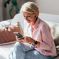 Eine Frau sitzt auf dem Sofa und schaut auf ihr Smartphone.