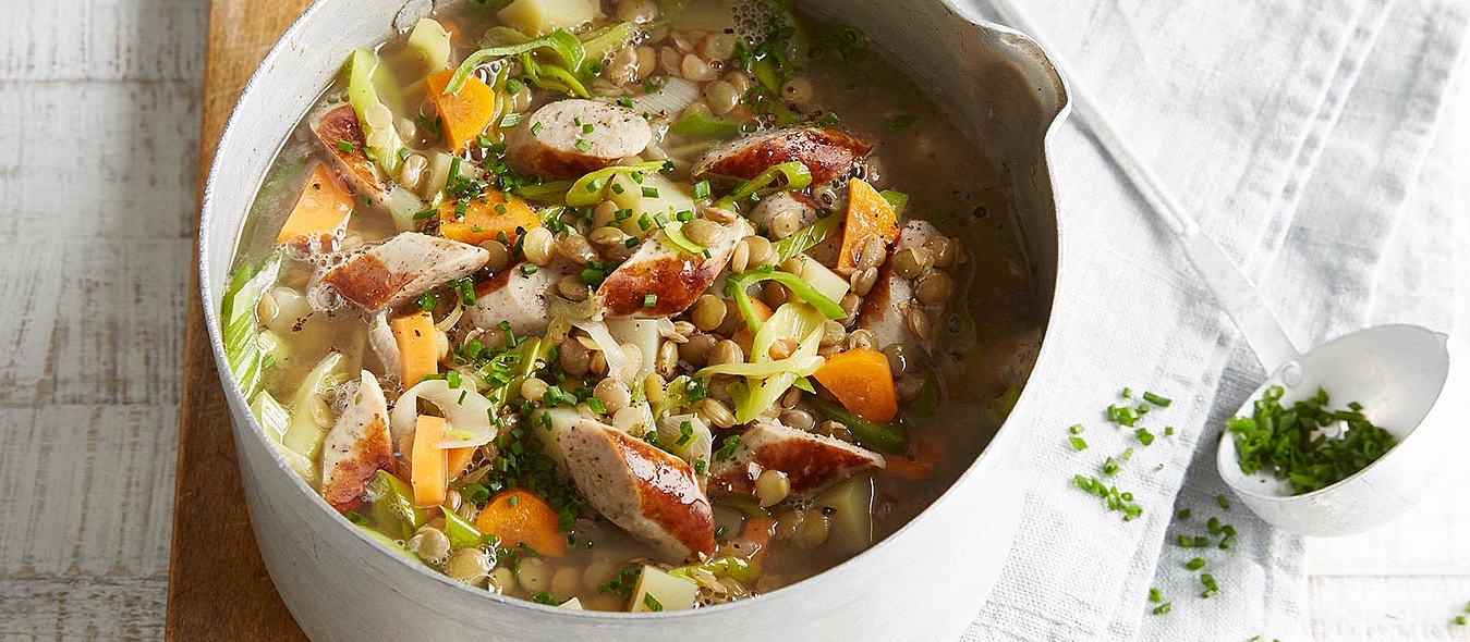 Kartoffel-Linsen-Eintopf mit Rostbratwürstchen und Gemüse in einem Kochtopf.