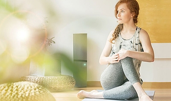 Eine junge Frau mit langen lockigen Haaren sitzt in Sportkleidung auf einer Yogamatte. Sie macht eine Hatha-Yoga-Pose.