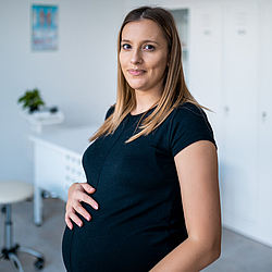 Eine schwangere Frau in einem schwarzen T-Shirt hat eine Hand auf ihren Bauch gelegt.