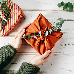 Zwei Hände halten ein Geschenk. Auf dem Geschenk liegt ein Zweig.